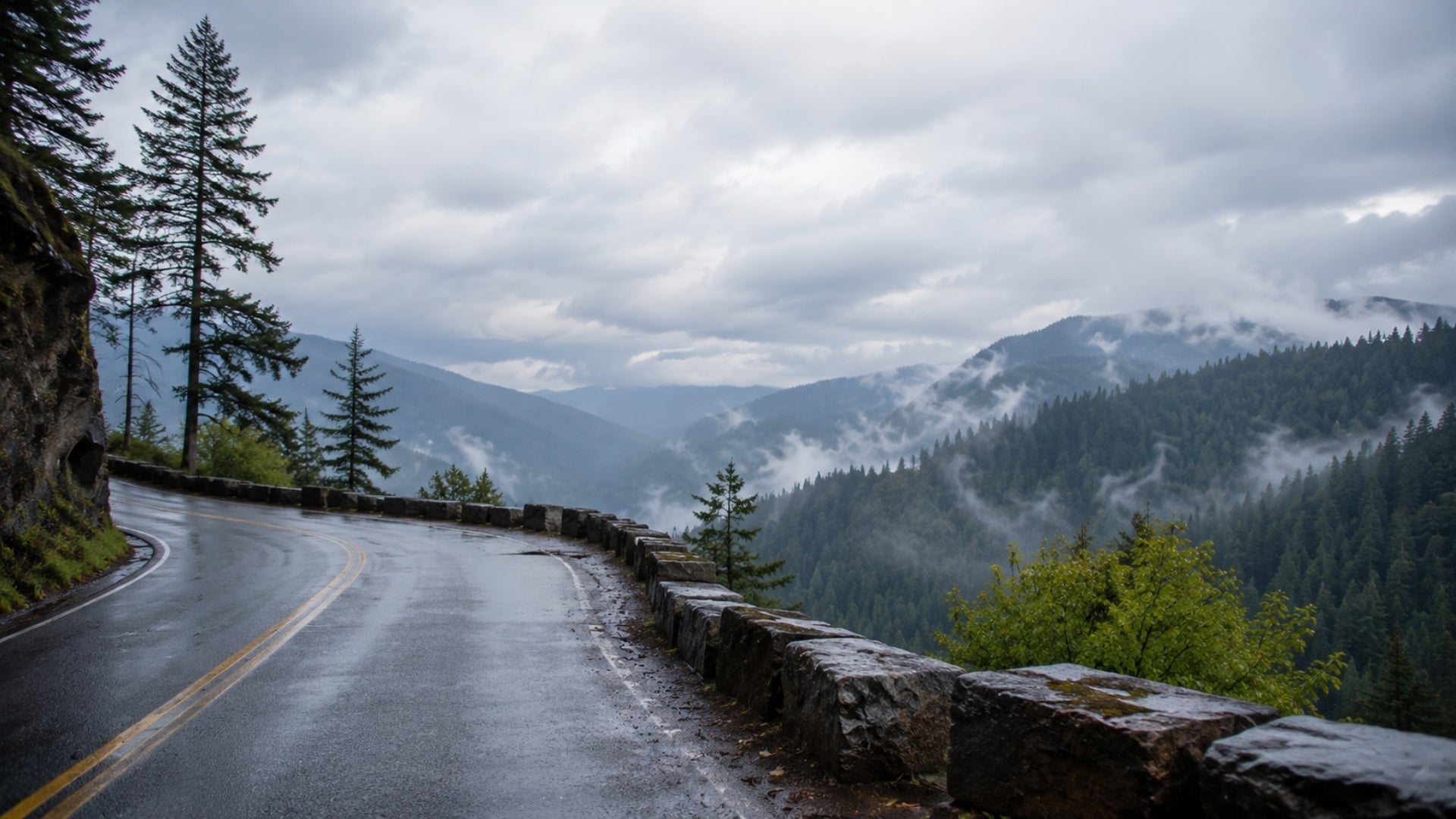Winding road through a mountainous landscape with trees and foggy mountains.